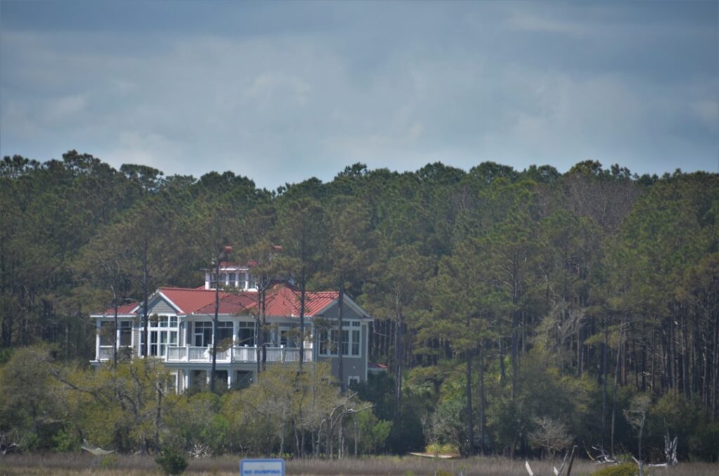 A luxurious coastal home with large windows and lush landscaping near palm trees and the water.