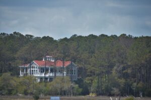 A luxurious coastal home with large windows and lush landscaping near palm trees and the water.