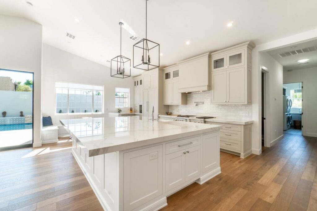 Agent and couple reviewing a luxury home listing with price comparisons on a kitchen counter.